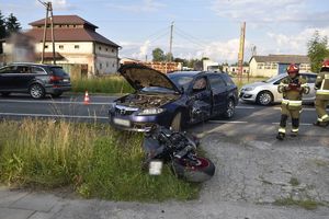 Miejsce wypadku. Na mostku lezy przewrócony motocykl, na drodze stoi niebieska mazda