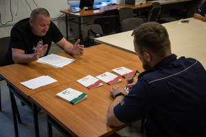 policjant i mężczyzna siedzą przy biurku, przed nimi leżą książki