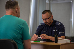 policjant w mundurze siedzi przy biurku, na przeciwko mężczyzna