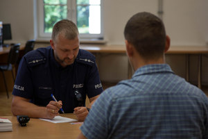 policjant siedzący przy biurku, na przeciwko mężczyzna