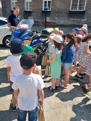 Dzieci stojące przed policyjnym motocyklem słuchają policjanta ruchu drogowego.