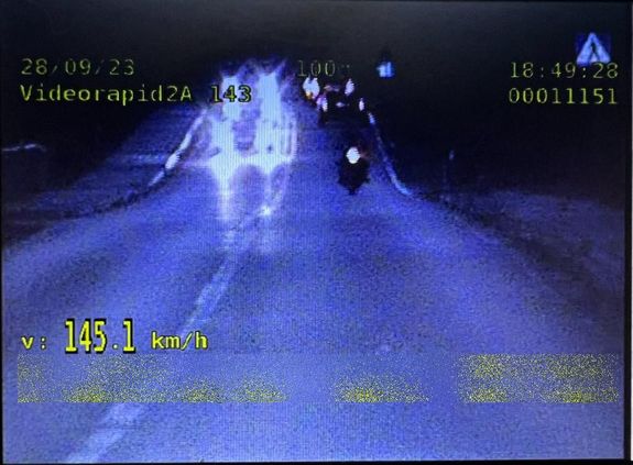 Zdjęcie motocyklisty jadącego drogą, po lewej stronie zarejestrowana jego prędkość 145,1 km/h. W górnej części zdjęcia data i godzina wykroczenia.