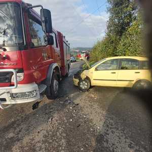 wóz straży pożarnej i zniszczony przód osobowej pandy na drodze asfaltowanej