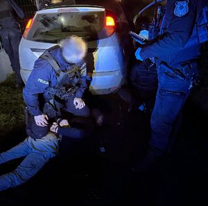 zatrzymany sprawca ucieczki, leżący na ziemi. w okół policjanci mundurowi