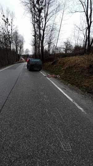 Tył ciemnego samochodu, na poboczu leży czerwony rower